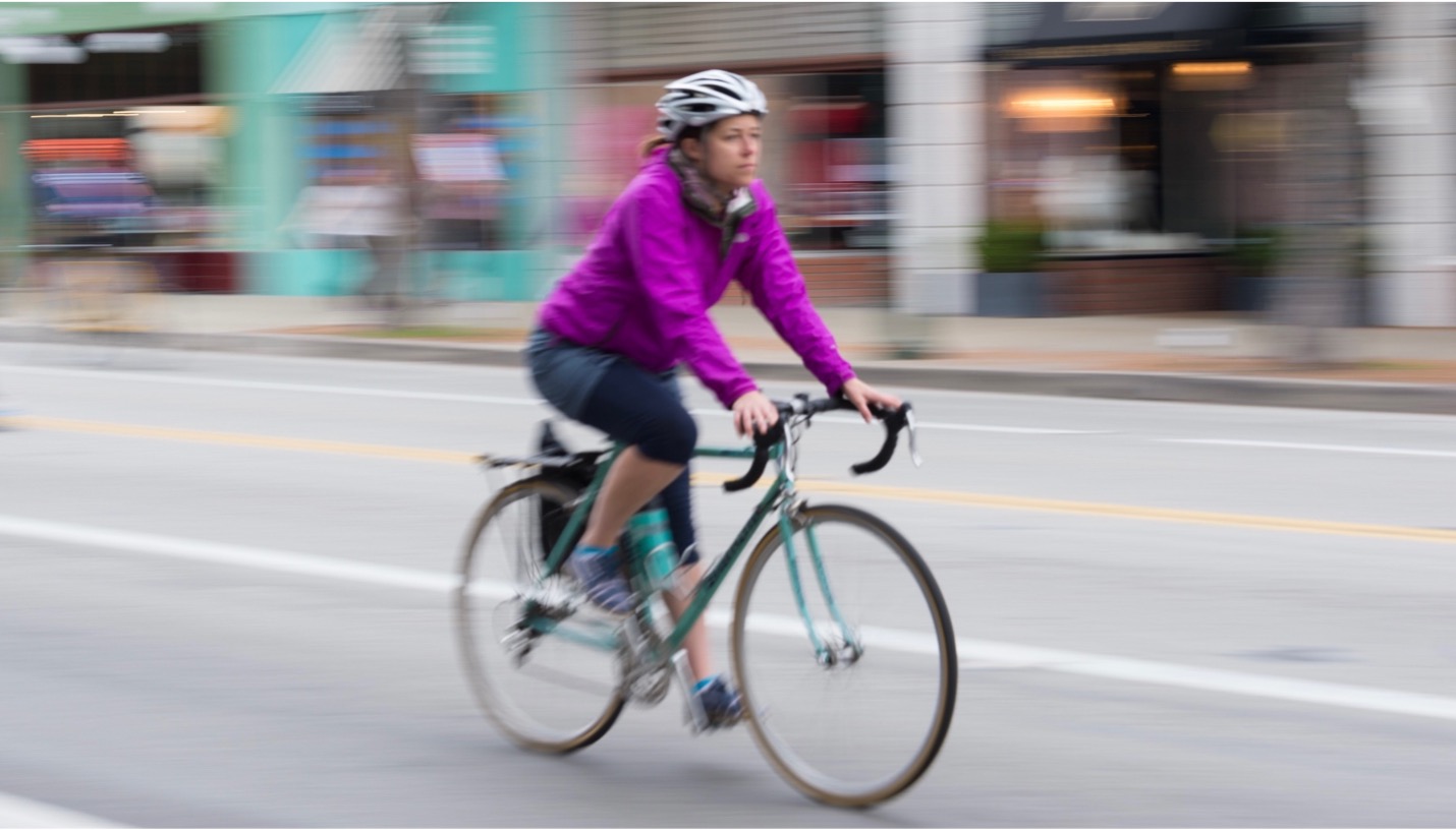 woman in pink jacket riding down a city street at speed.